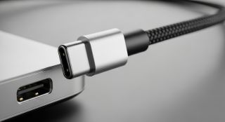 Close up of a usb type c cable plugged into a laptop port on a gray surface